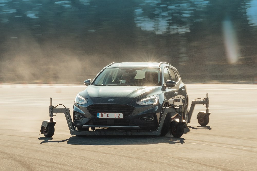 Een grijze Ford Focus met testapparatuur rijdt over een circuit, met stof opwaaiend erachter.