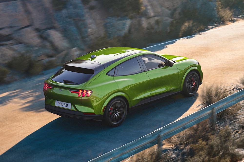 Groene Ford Mustang Mach-E in volle vaart op een bochtige bergweg.