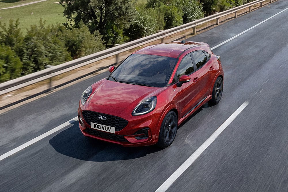 Rode Ford Puma rijdend op een weg langs een groene omgeving