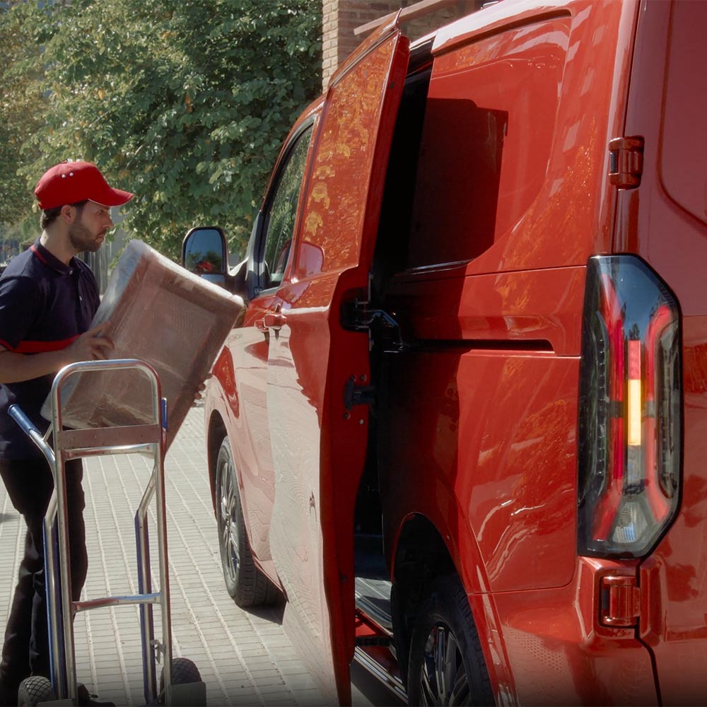 De bezorger lost pakketten van een rode Ford Transit Custom.