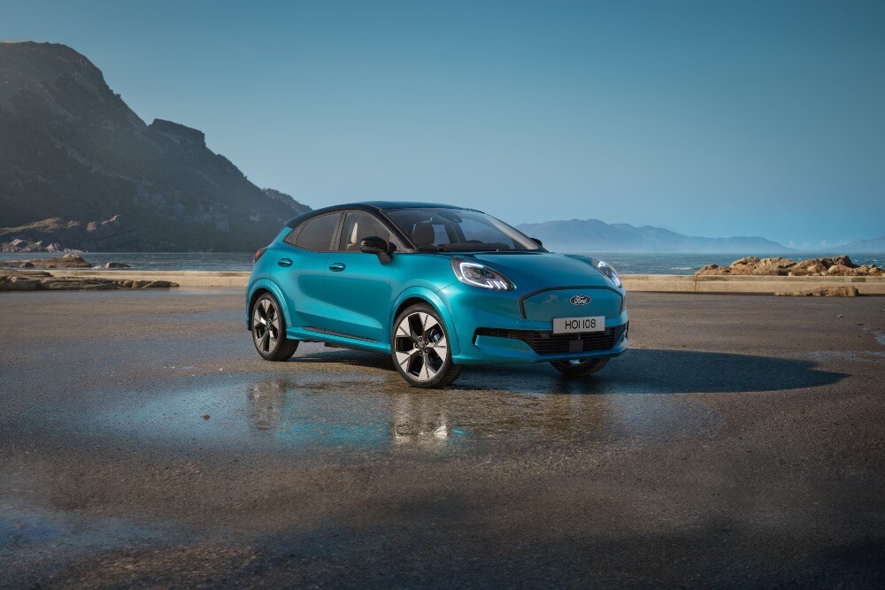 Een blauwe Ford Puma Gen-E op een nat strand onder een blauwe hemel. 
