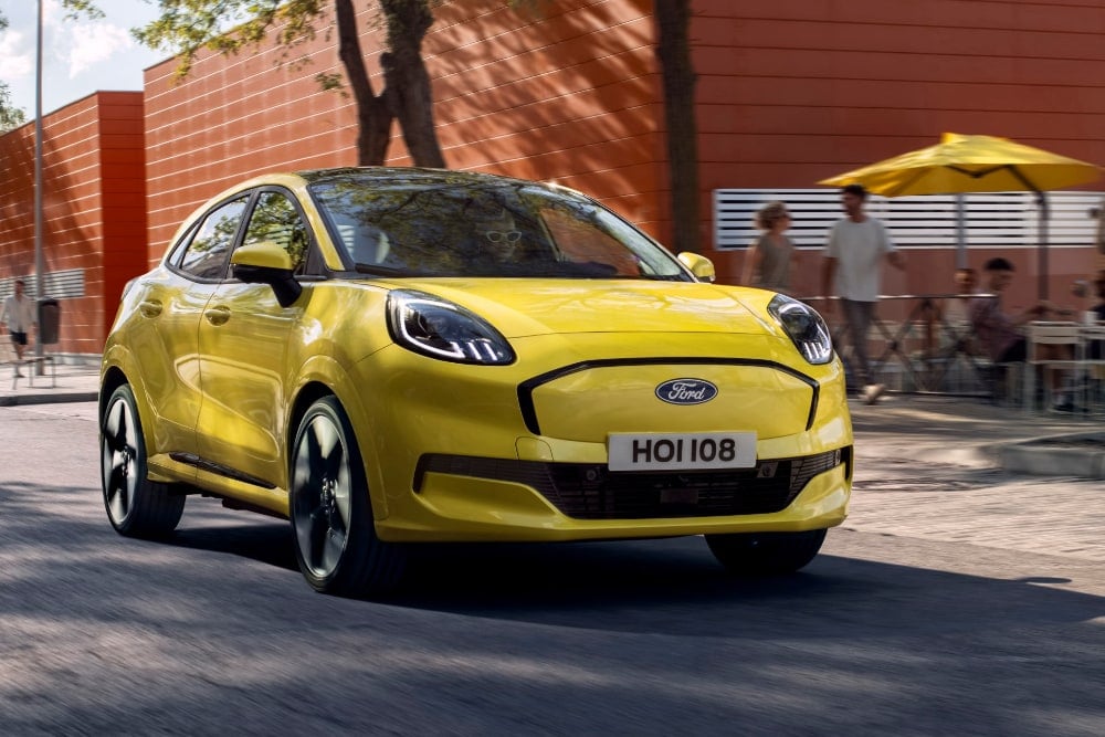 Een gele Puma Gen-E die voorbij een café met terras rijdt.