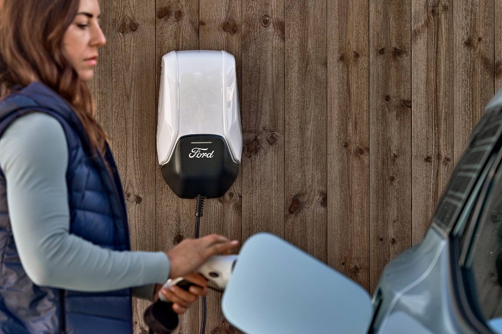 Een vrouw sluit haar blauwe elektrische Ford Explorer aan op een thuislaadpunt.