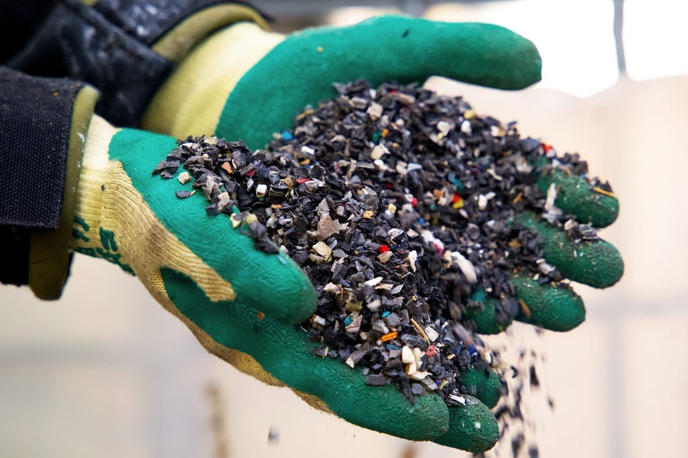 Handen in rubberen handschoenen houden stukken gerecycled plastic afval vast.