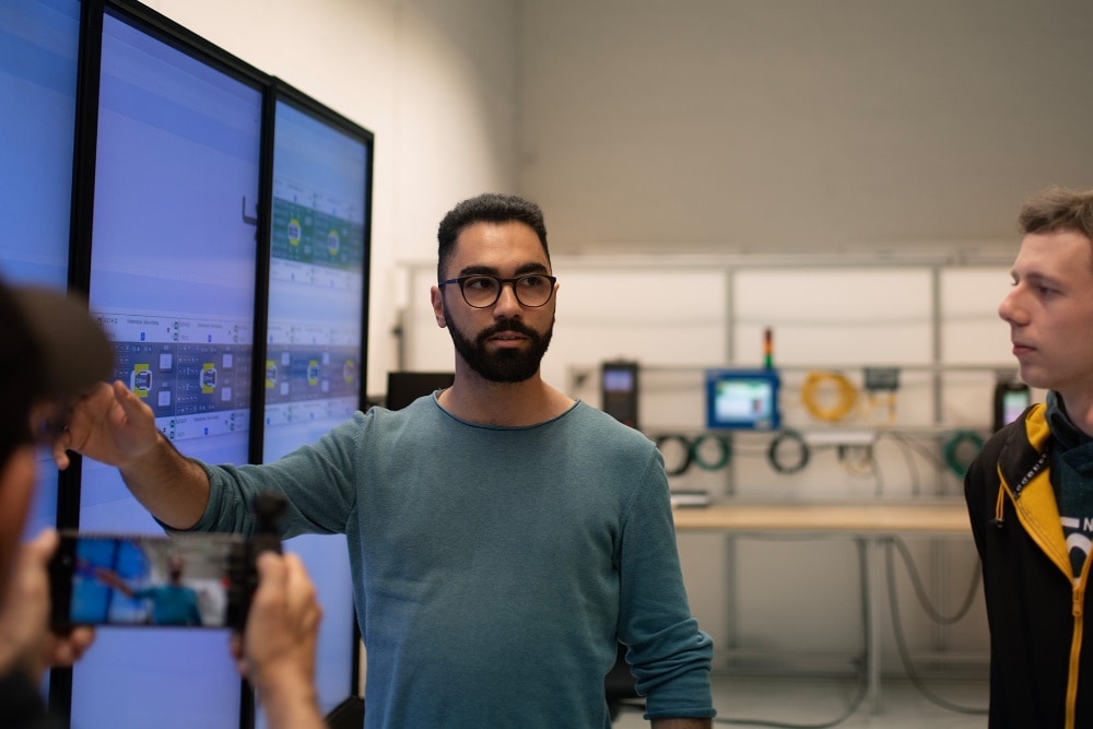 Een groep Ford-collega's houdt een staande vergadering rond een digitaal scherm.