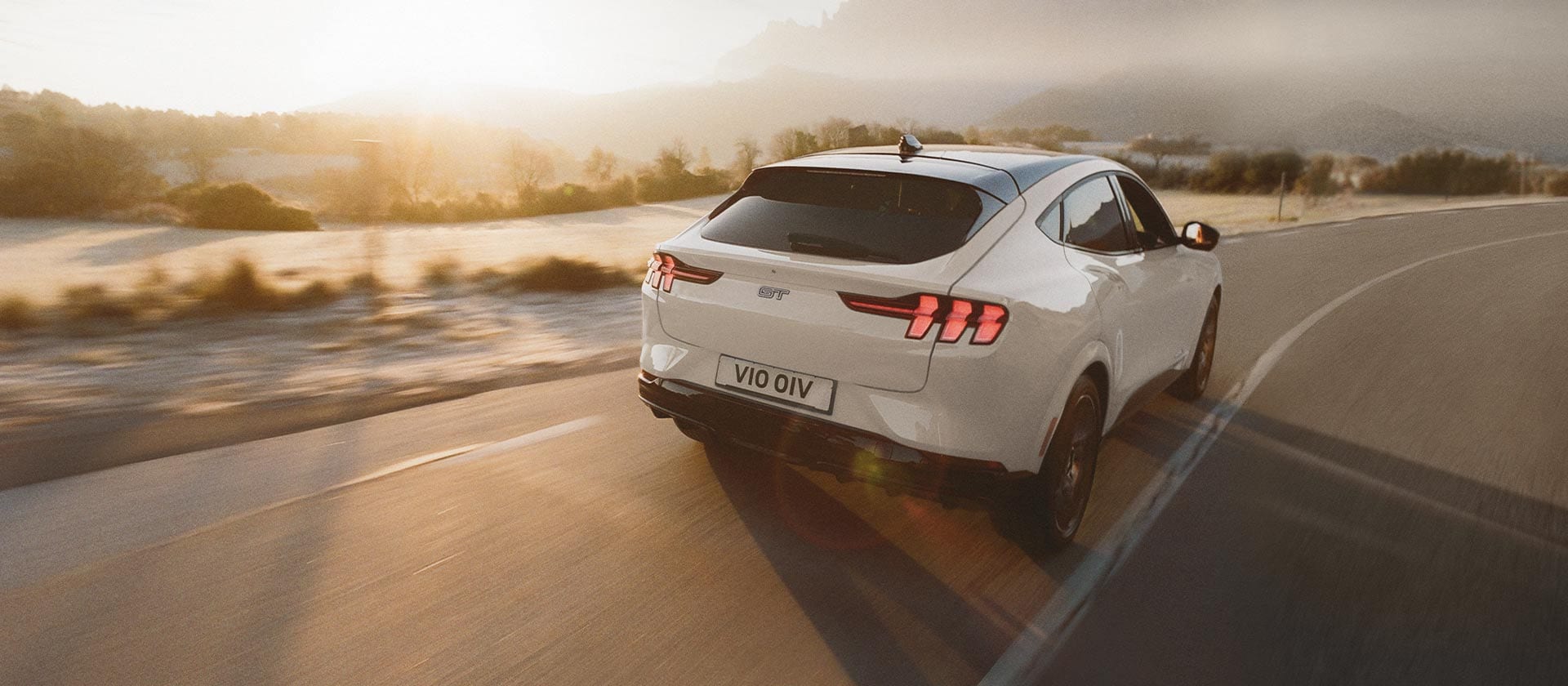 A silver Ford Mustang Mach-E electric vehicle driving on a long open road. 