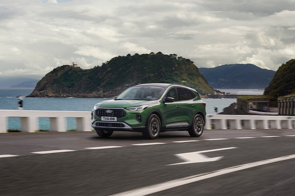 Een groene Ford Kuga zelfopladende hybride auto die langs een schilderachtige weg rijdt.
