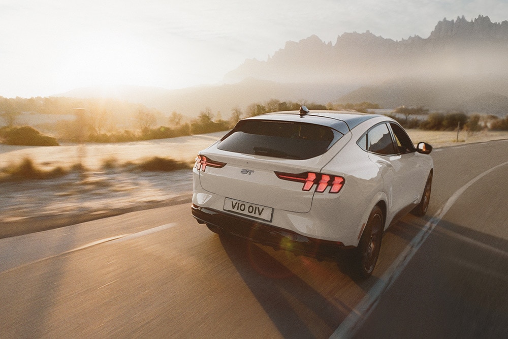 Een zilveren elektrische Ford Mustang Mach-E GT die langs een schilderachtige weg rijdt.