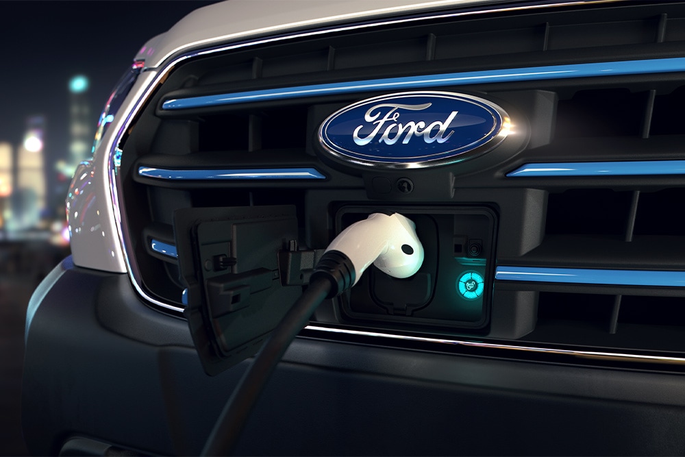Close-up van een Ford E-Transit bestelwagen oplaadpunt en het blauwe ovale Ford-embleem op de voorkant van de grille.