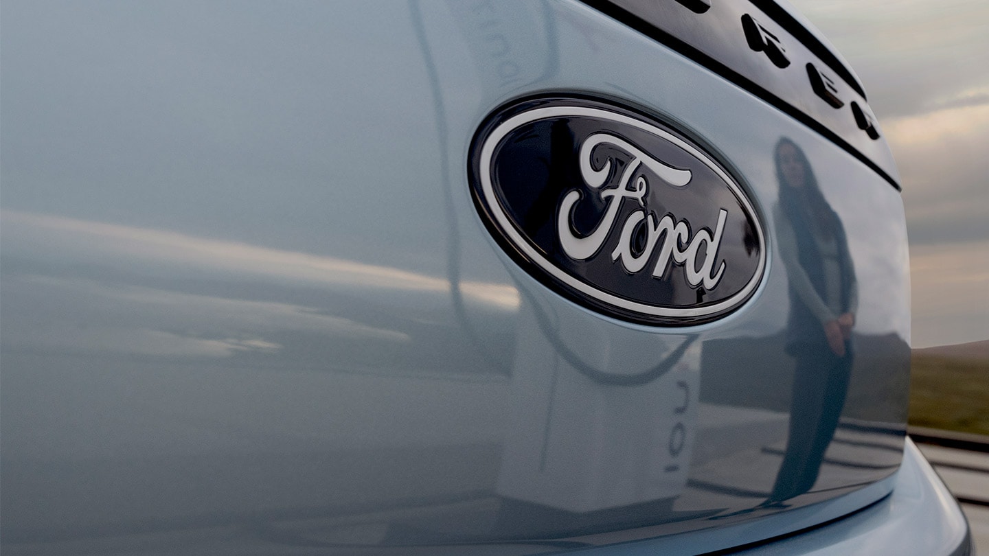 Ford-logo op een blauwe elektrische Ford Explorer met een openbare laadpaal weerspiegeld in de auto.