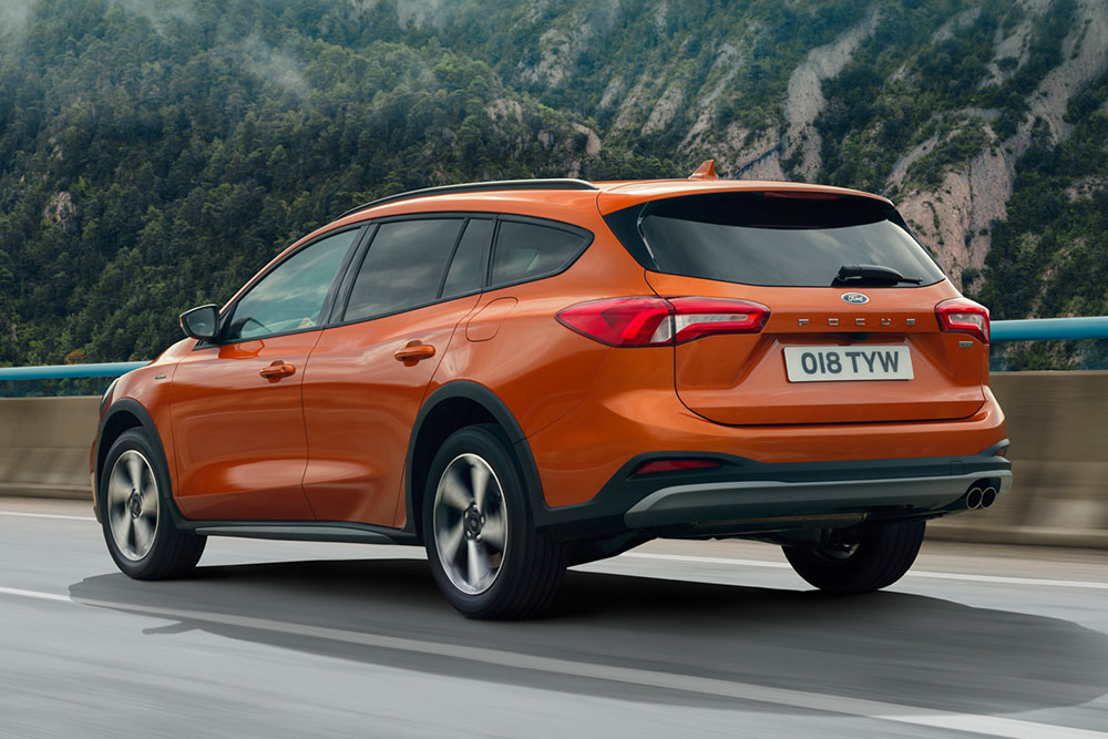 Achter 3/4 zicht van een oranje Ford Focus op een mistige bergweg.