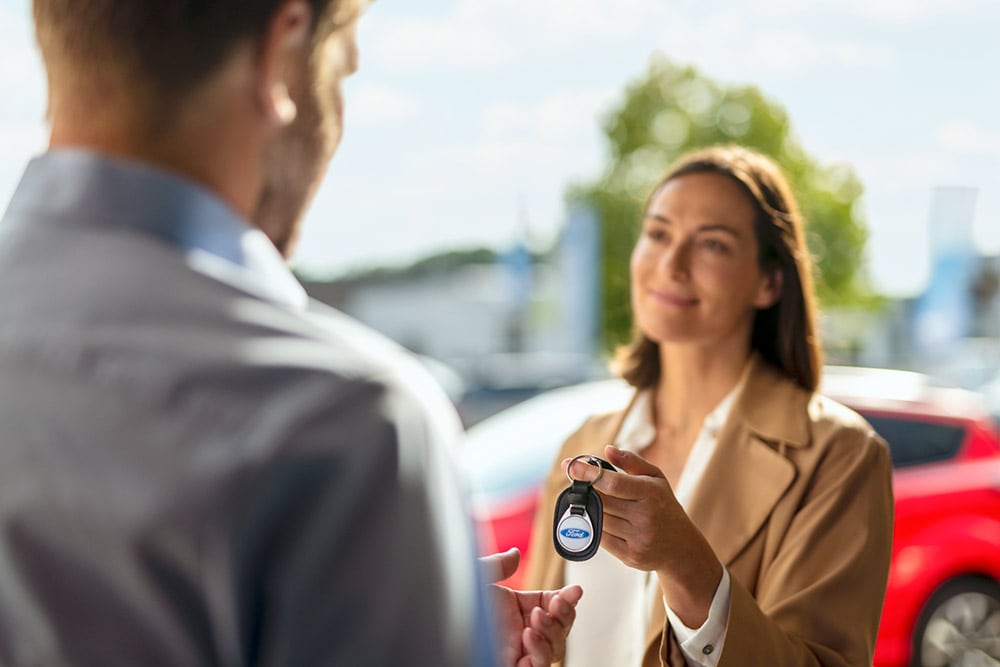 Een vrouw overhandigt autosleutels met Ford-logo aan een man.