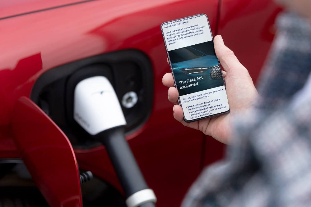 Een persoon leest uitleg over de Wetgeving inzake gegevensbescherming op zijn telefoon naast een elektrisch voertuig dat wordt opgeladen.