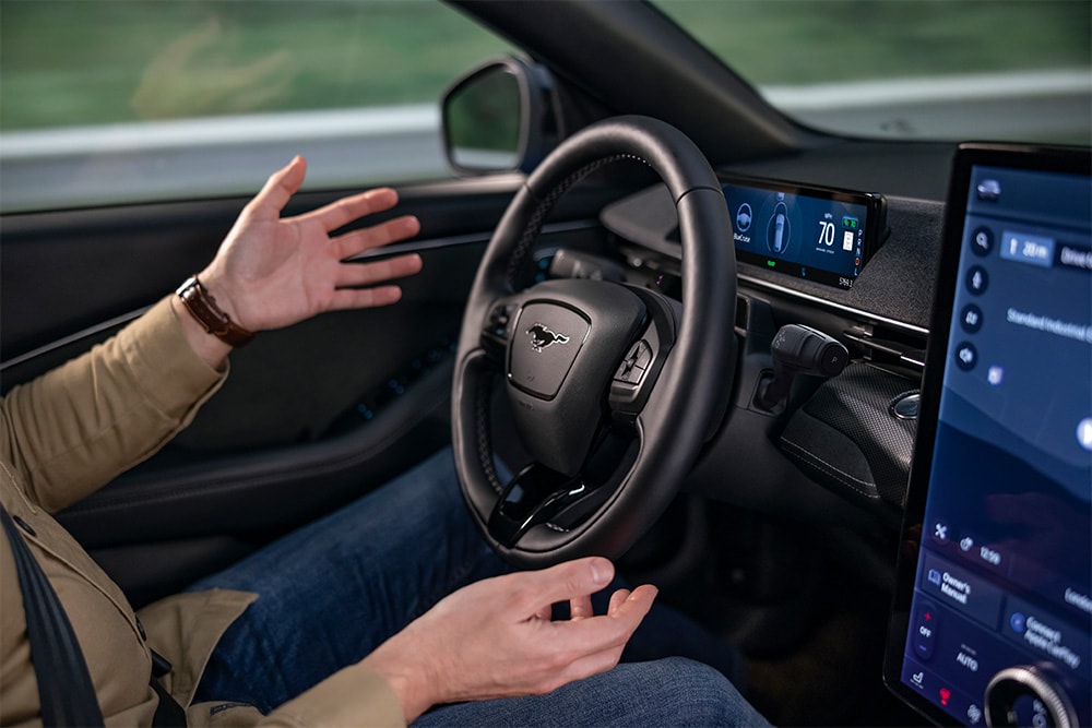 Handen over het stuur van de Mustang Mach-E met een beeld van de BlueCruise-technologie voor autonoom rijden