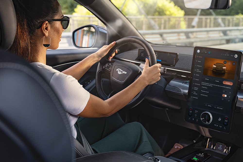 Een vrouw bestuurt de Mustang Mach-E met haar handen aan het stuur. Het 15.5" touchscreen toont details over de auto.