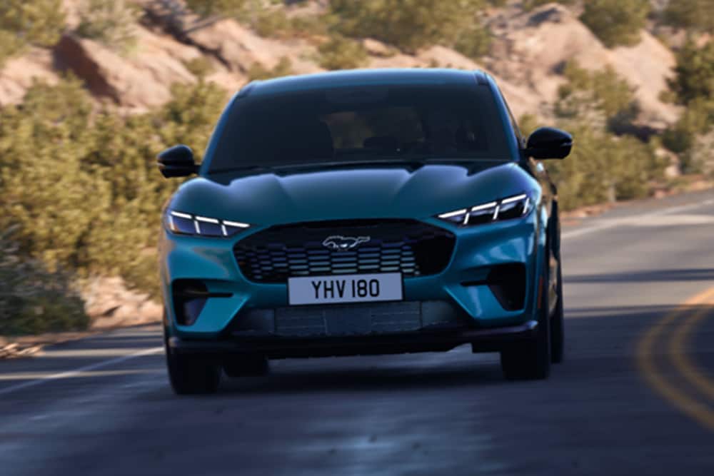 Vooraanzicht van een blauwe Ford Mustang Mach-E op bergweg.