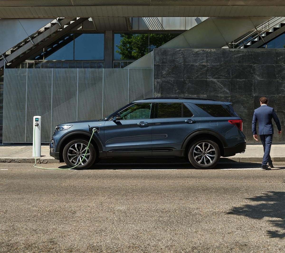 Side view of Ford Explorer PHEV parking next to the charging point with person walking around