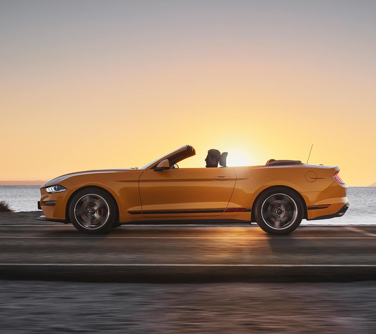 Ford Mustang California Edition driving on a highway against a sunset backdrop.
