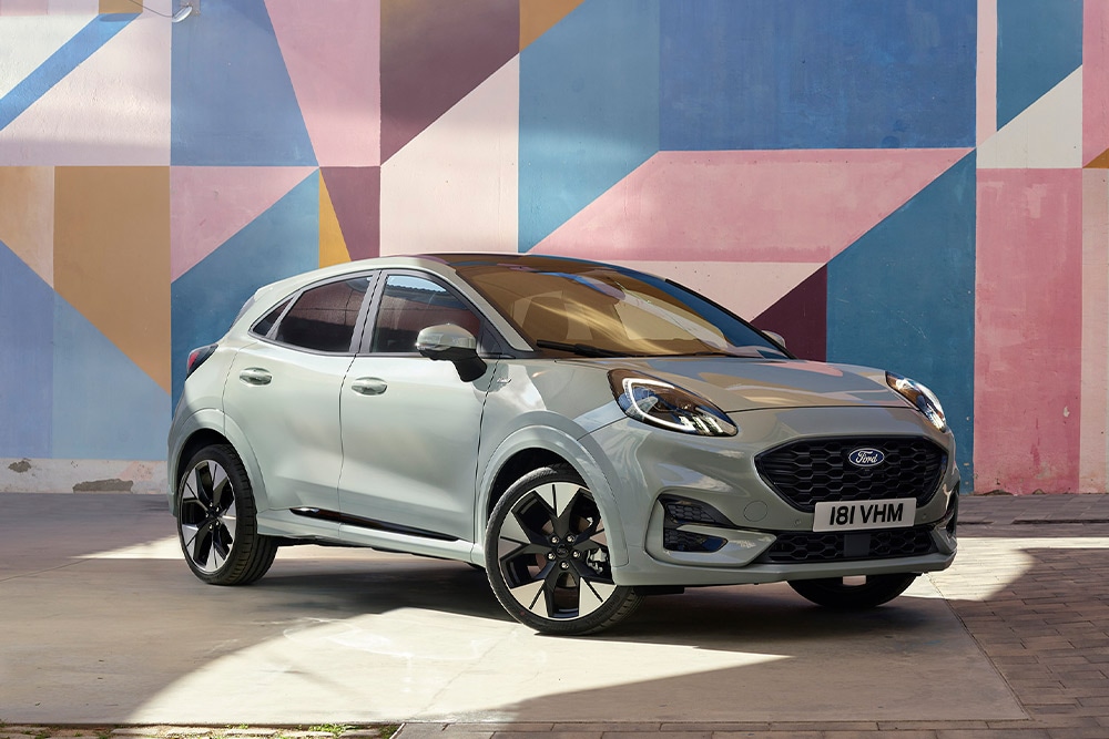 Een zilverkleurige Ford Puma SUV geparkeerd voor een kleurrijke geometrische muurschildering.