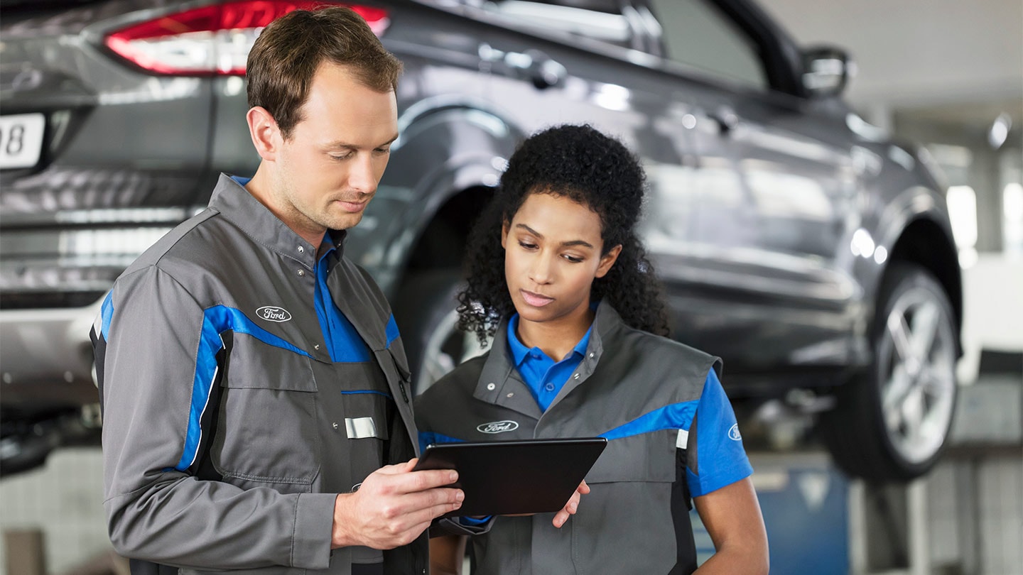 Twee Ford reparatiespecialisten controleren hun online serviceboekingssysteem op een telefoon.
