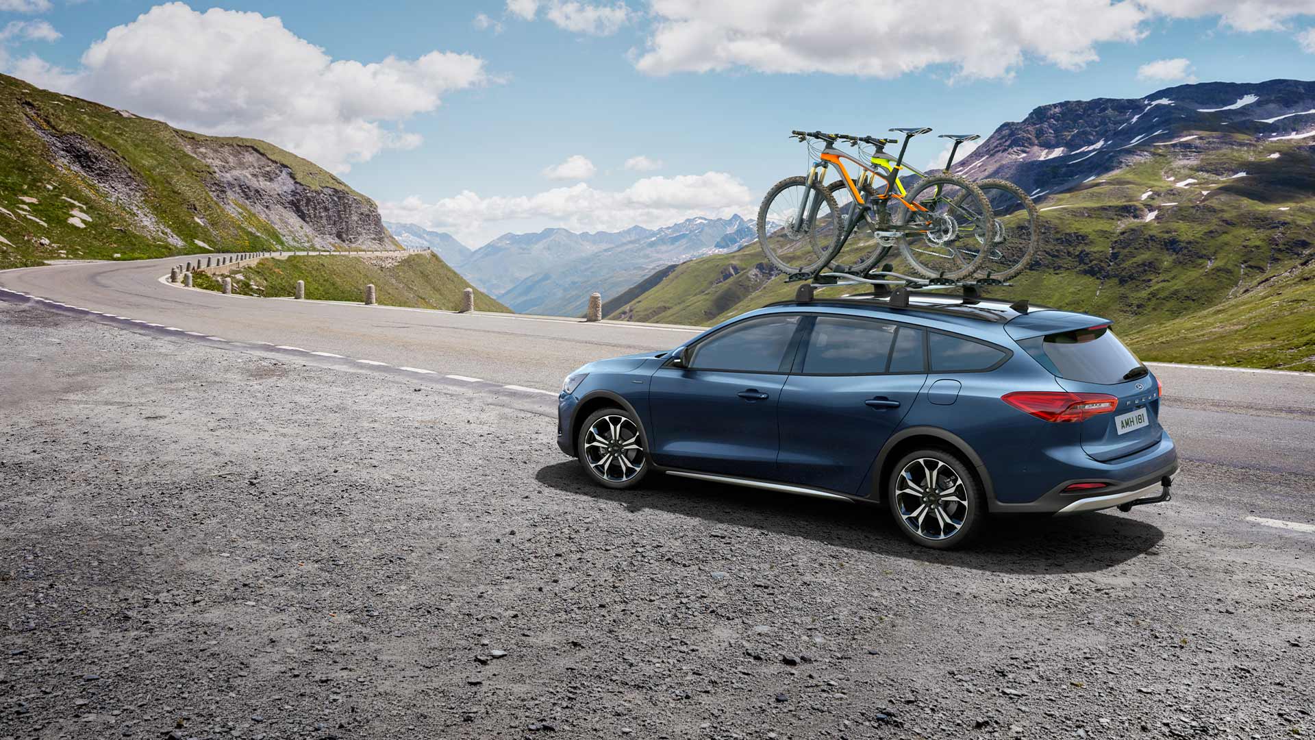 Een blauwe Ford Focus met fietsen op het dak rijdt over een panoramische bergweg.