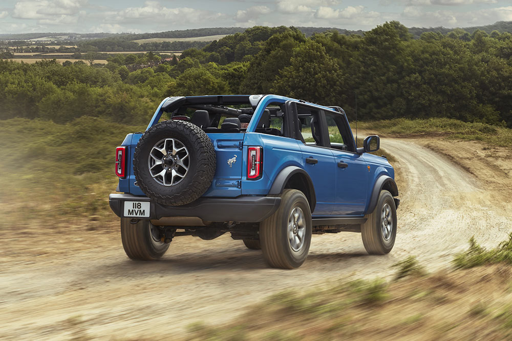 Een achteraanzicht van een blauwe Ford Bronco door een landelijk landschap.