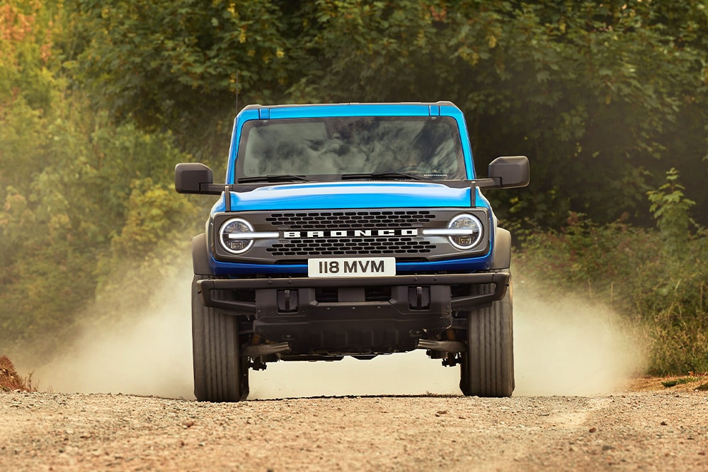 Vooraanzicht van een blauwe Ford Bronco op een onverharde weg. 