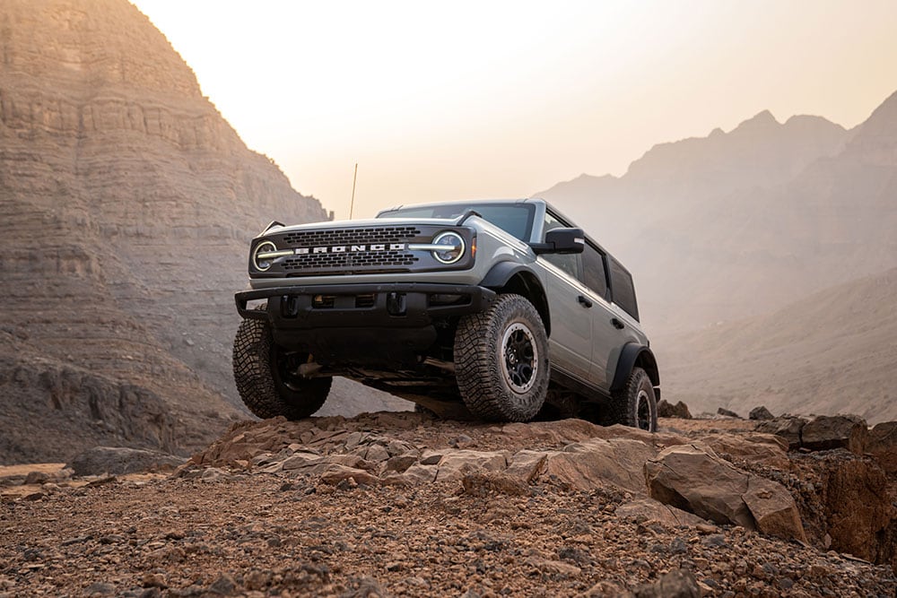 Een grijze Ford Bronco geparkeerd op een rotsachtig pad in een bergachtige omgeving.