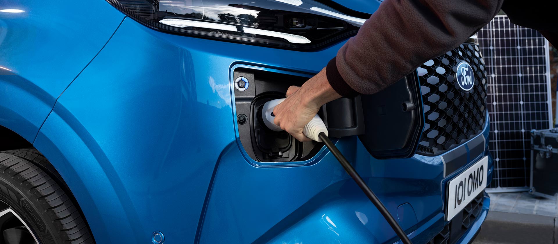 Een hand steekt een oplaadkabel in een blauwe Ford E-Tourneo Custom.