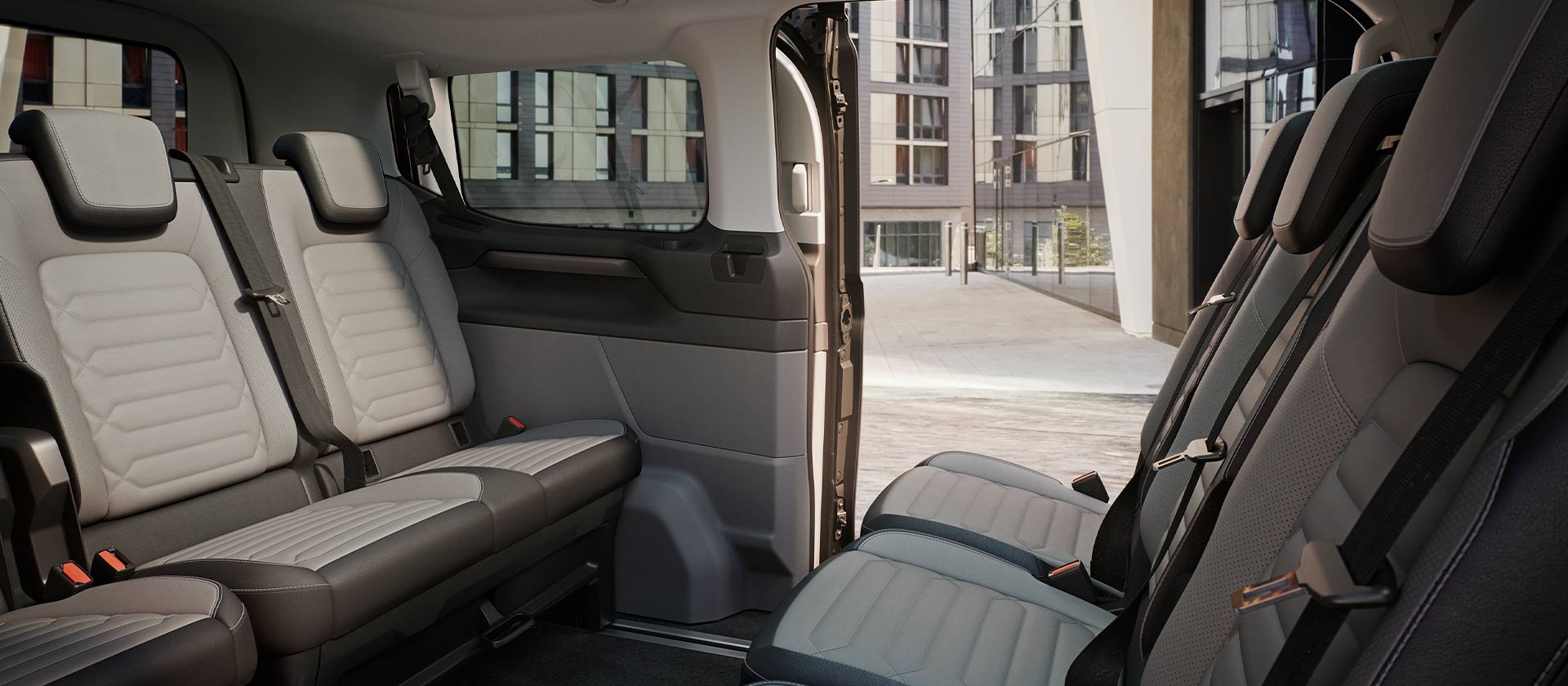 Binnenaanzicht van de Ford Tourneo Custom, met meerdere rijen grijze passagierszetels en een panoramisch zonnedak.