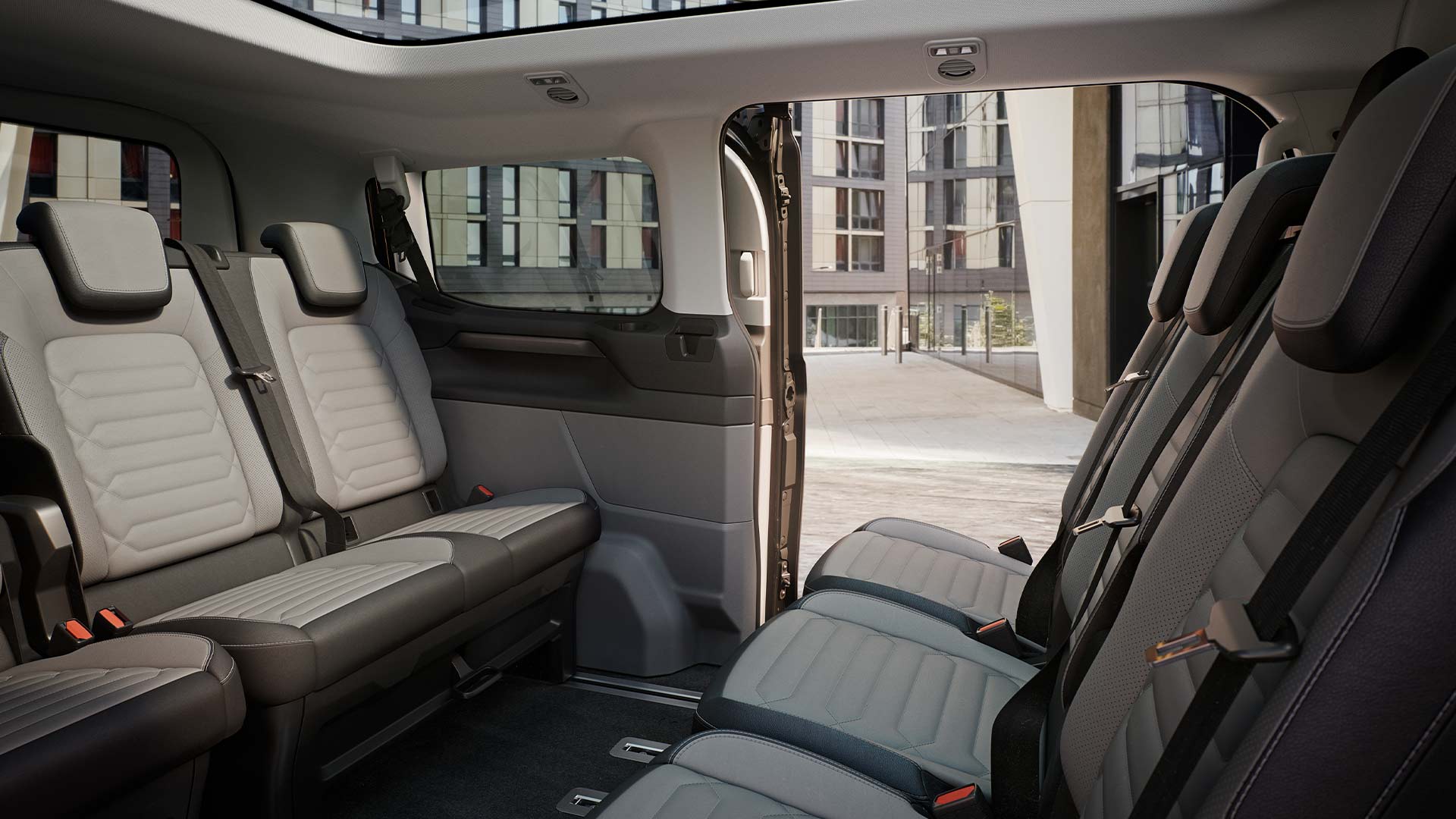 Binnenaanzicht van de Ford Tourneo Custom, met meerdere rijen grijze passagierszetels en een panoramisch zonnedak.
