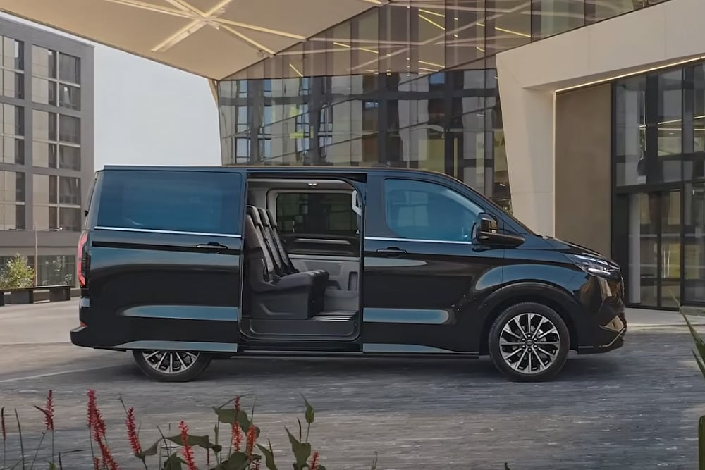 Een zwarte Ford E-Tourneo Custom staat geparkeerd met de zijdeur open, waardoor de interieurzetels zichtbaar worden.