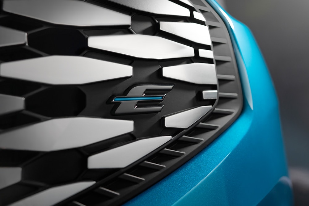 Close-up van de grille van de Ford E-Tourneo Custom, met het blauwe "E"-logo, exclusief voor elektrische voertuigen van Ford.
