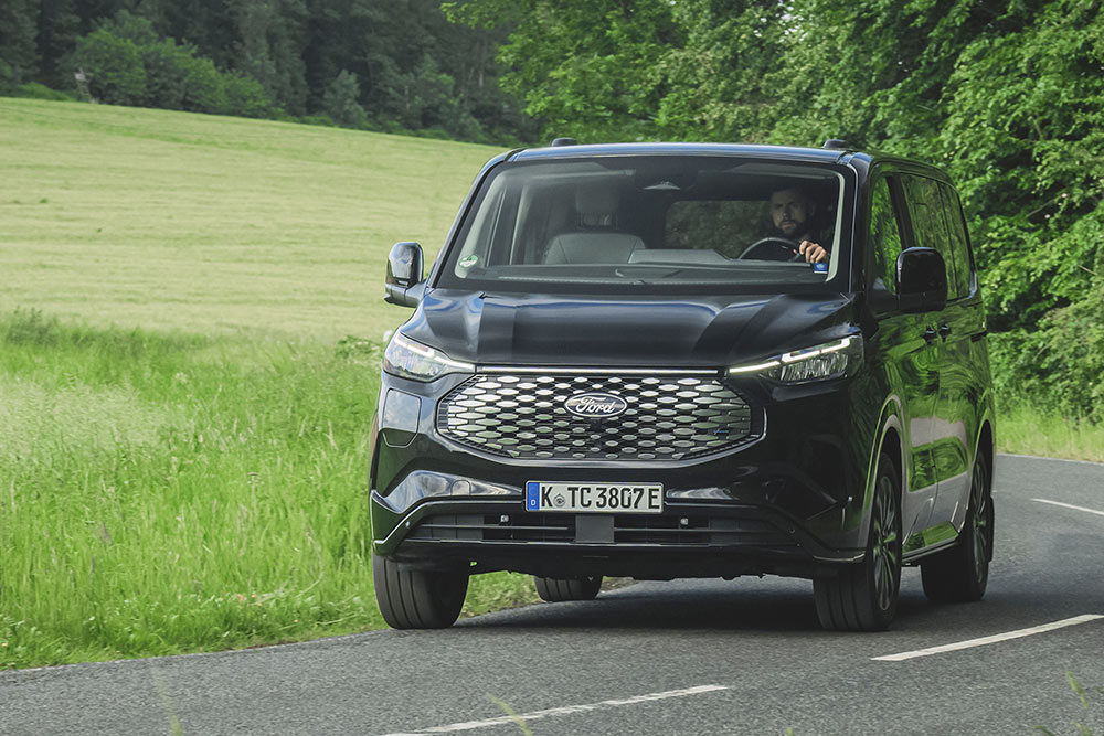 Een zwarte Ford E-Tourneo Custom rijdt op een landelijke weg.