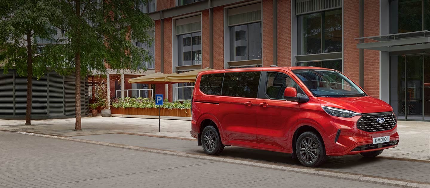 Een rode Ford Tourneo Custom staat geparkeerd in een stadsstraat.