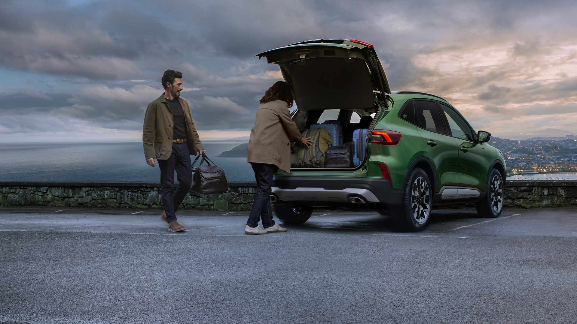 Twee mensen laden meerdere koffers in de ruime kofferruimte van de Ford Kuga. 