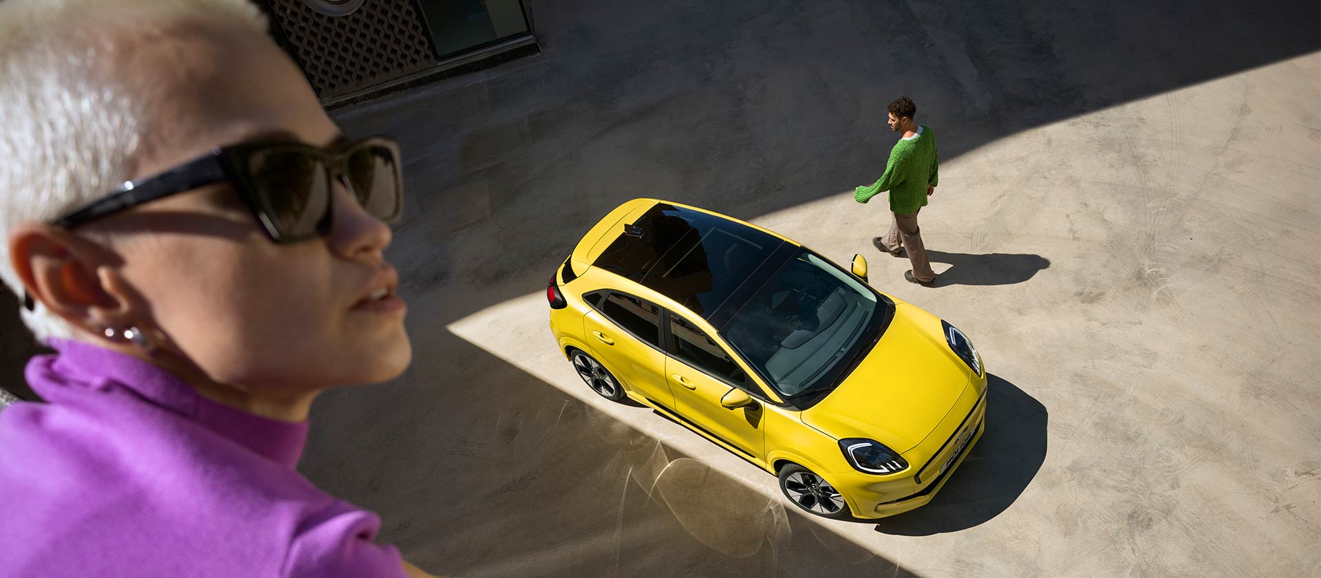 Vogelperspectief van een gele elektrische Ford Puma Gen-E®. Persoon in paars op de voorgrond.