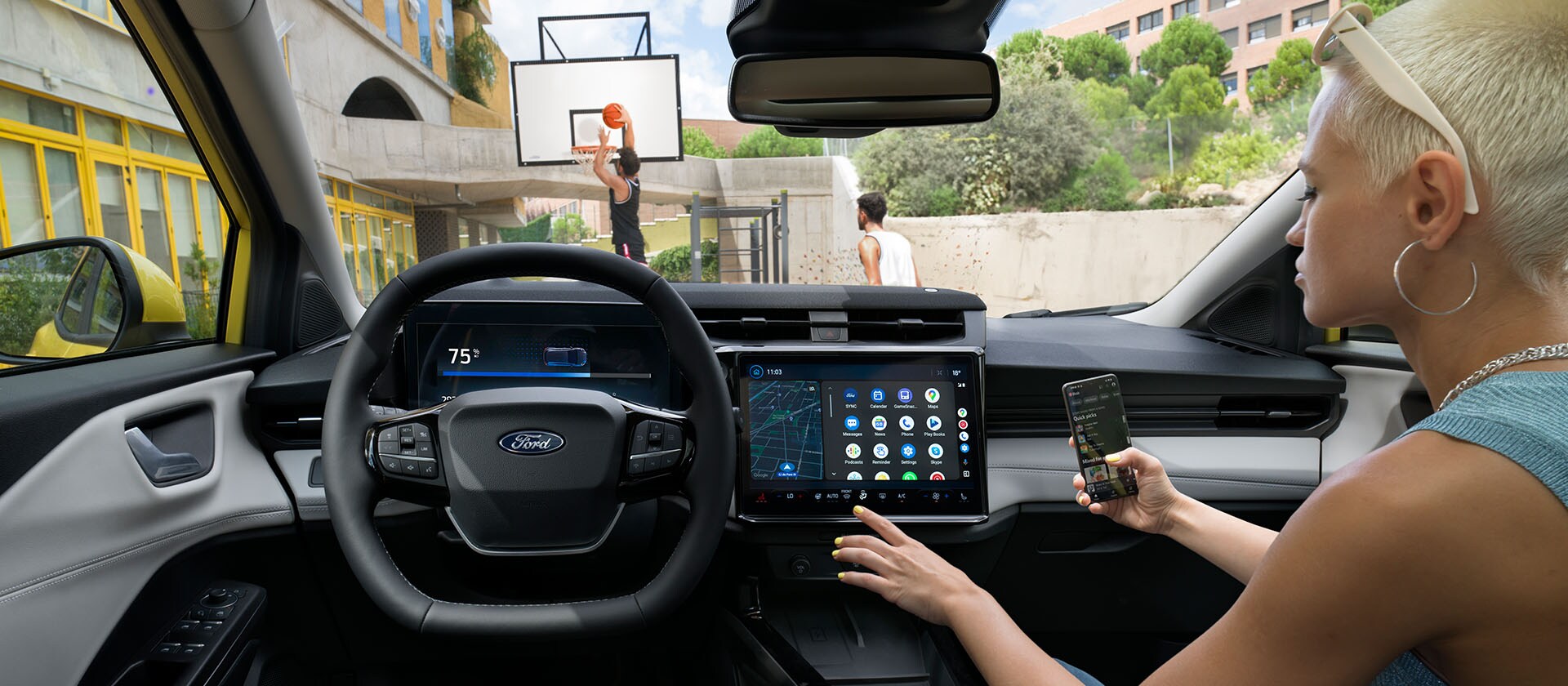 Het interieur van de elektrische Ford Puma Gen-E®, met een persoon die zijn mobiele telefoon draadloos synchroniseert met het grote touchscreen.