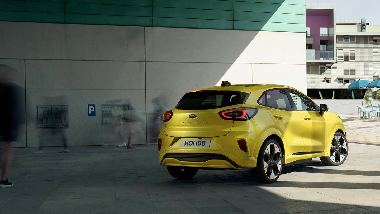 De achterhoek van een gele elektrische Ford Puma Gen-E® geparkeerd onder een brug.
