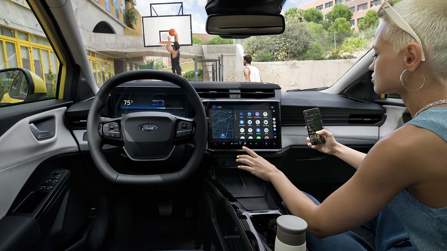 Het interieur van de elektrische Ford Puma Gen-E®, met een persoon die zijn mobiele telefoon draadloos synchroniseert met het grote touchscreen.