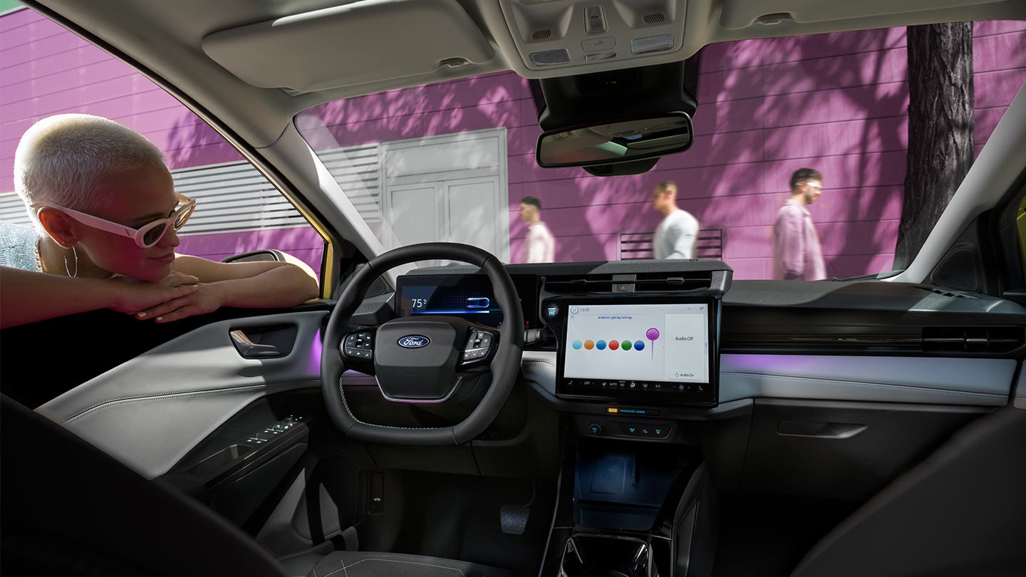Persoon die naar het interieur van de nieuwe Ford Puma Gen-E® kijkt en het grote touchscreen en de sfeerverlichting laat zien.