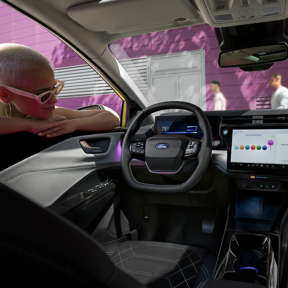 Het interieur van de elektrische Ford Puma Gen-E®, met een persoon die door het raam naar het grote infotainmentscherm kijkt.