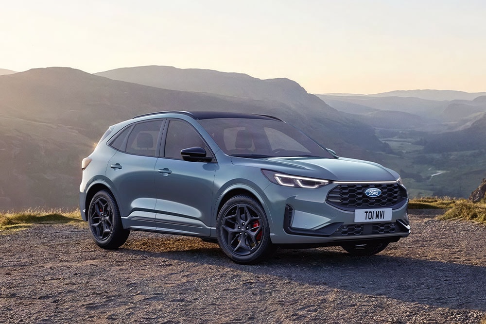 Een grijze Ford Kuga geparkeerd op een onverharde bergweg bij zonsondergang.