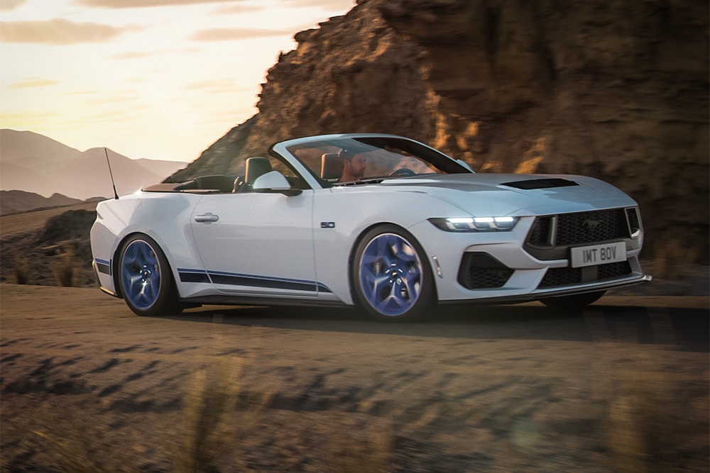 Zijprofiel van een witte Ford Mustang California Special op een weg tussen de heuvels