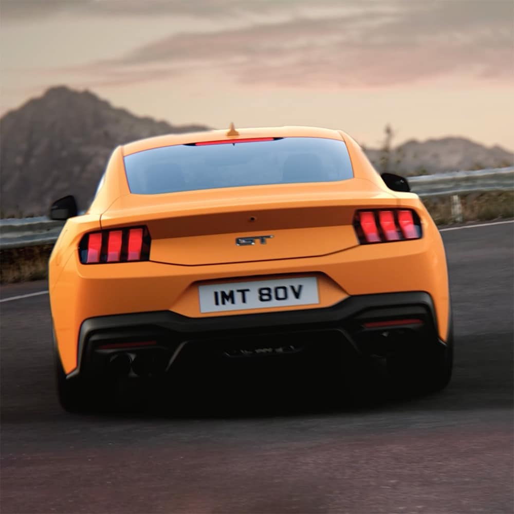 De achterkant van een Ford Mustang GT Fastback in Orange Fury die een scherpe bocht neemt op een landweg