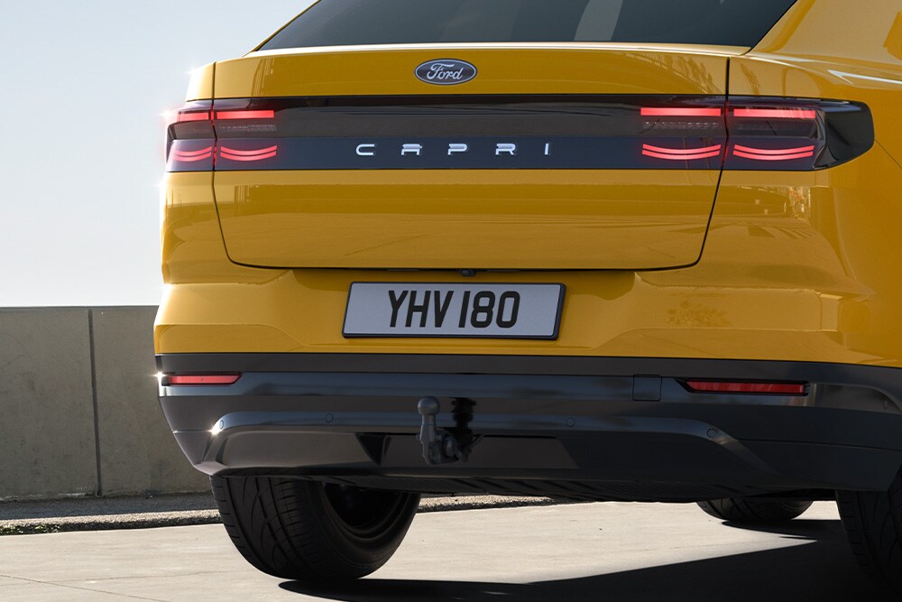 Achteraanzicht van een gele Ford Capri® die over een weg in de stad rijdt.