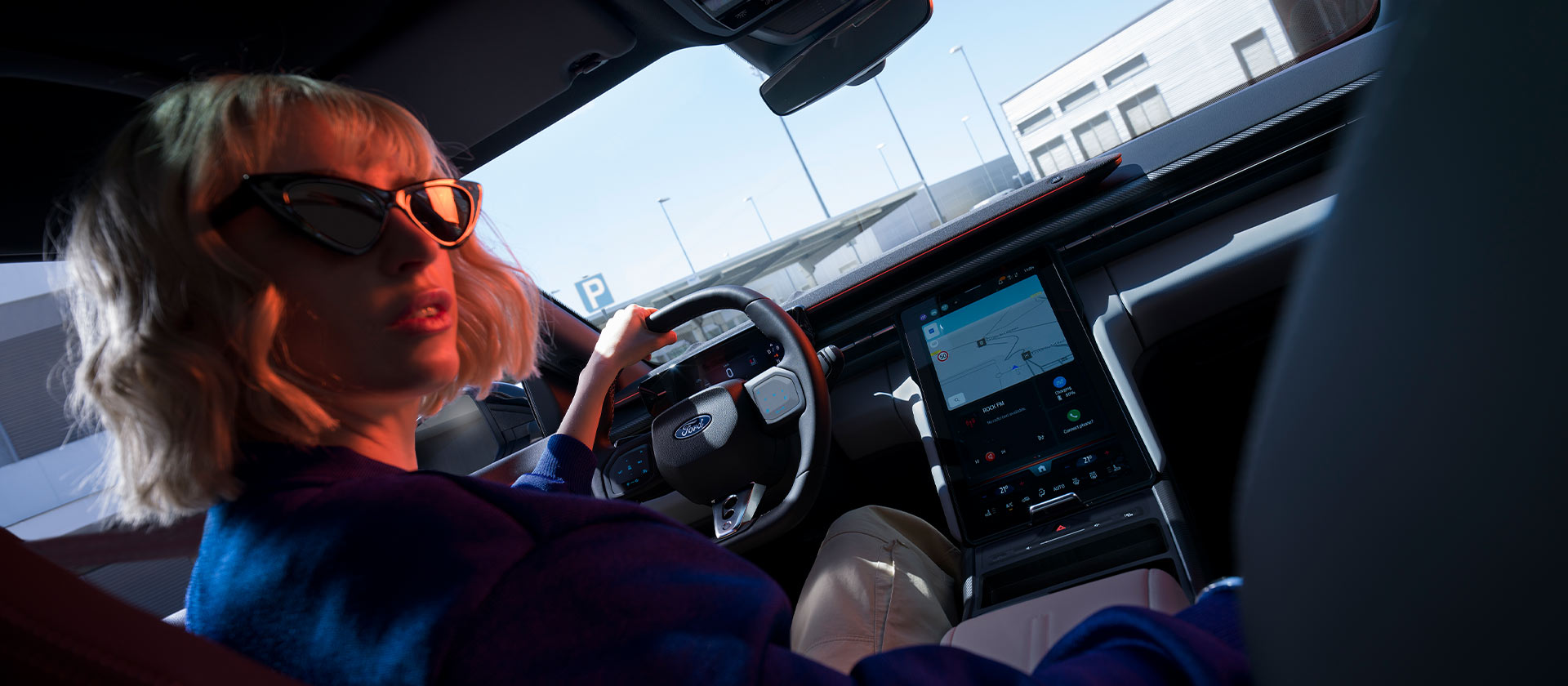 Een vrouw zit op de bestuurderszetel van een geparkeerde Ford Capri®, met zicht op het stuur en een groot SYNC® Move-touchscreen.