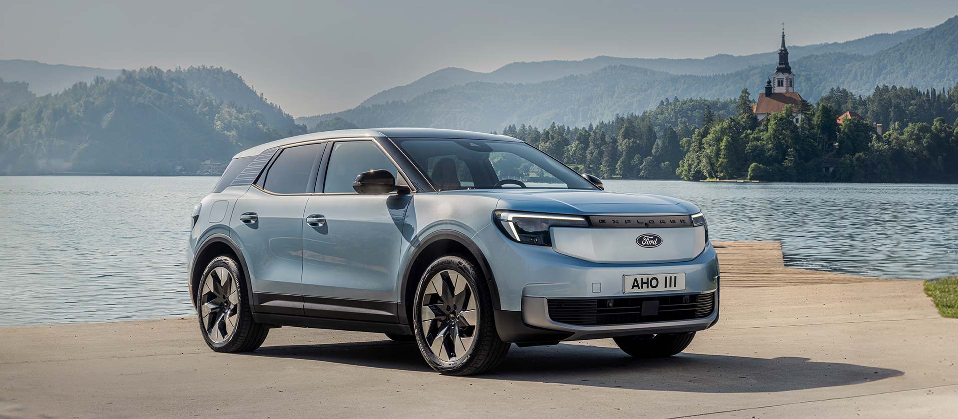 De nieuwe 100% elektrische Ford Explorer® in Arctic Blue, geparkeerd aan een meer.