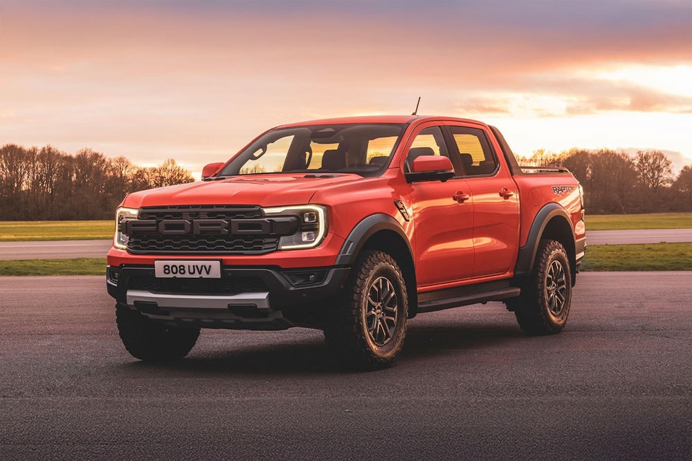 Een oranje Ford Ranger Raptor pick-up truck geparkeerd in een schilderachtig landschap.