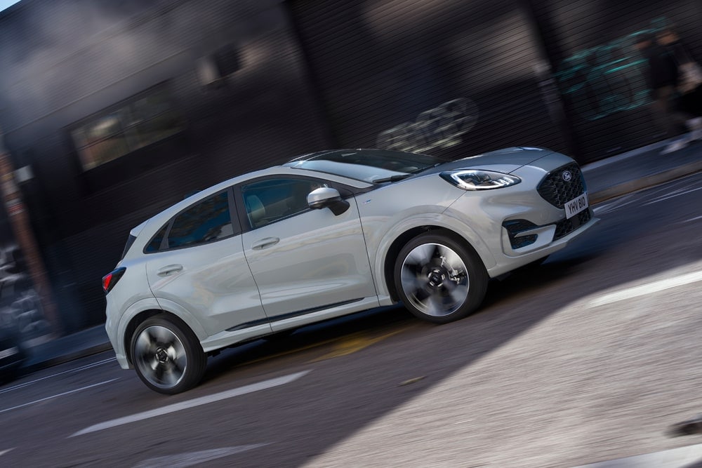 Zilverkleurige Ford Puma uit de serie kleine auto's van Ford rijdt over een stadsstraat.
